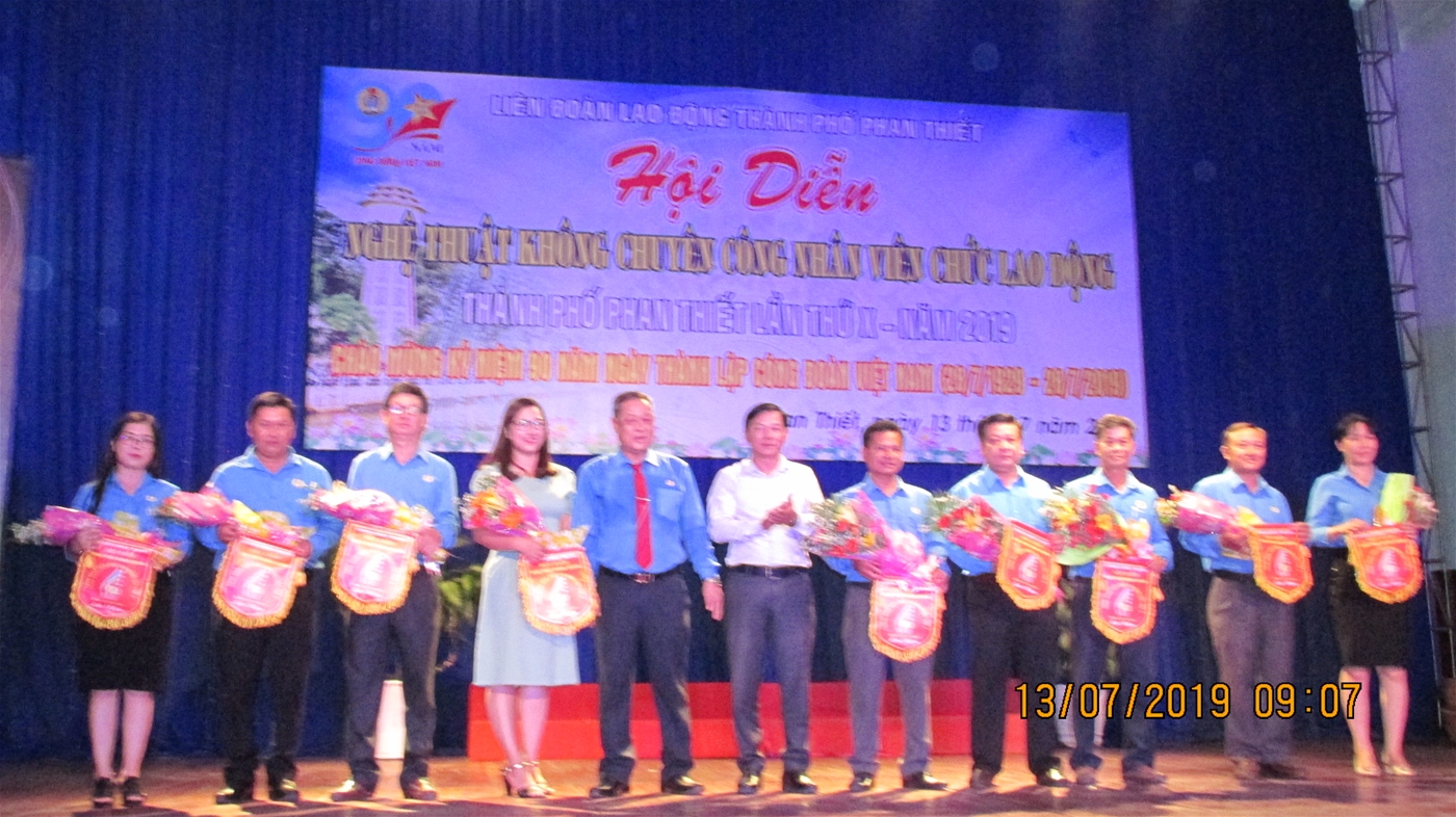 Ảnh: Ông Võ Huy Luận – Chủ tịch LĐLĐ thành phố - Trưởng BTC, Ông Trần Minh Tâm - Trưởng phòng VHTT – Phó Ban tổ chức tặng hoa và cờ cho các đội tham dự Hội diễn